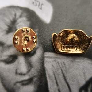 May include: Gold-toned metal pin with a raised design of a crown and the word "CREST" in all caps. The back of the pin has a circular design with a small hole in the center.