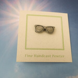 Puede incluir: Un pin de peltre plateado con forma de gafas de sol. El pin est&aacute; en una tarjeta blanca con ribete verde y el texto "Fine Handcast Pewter".