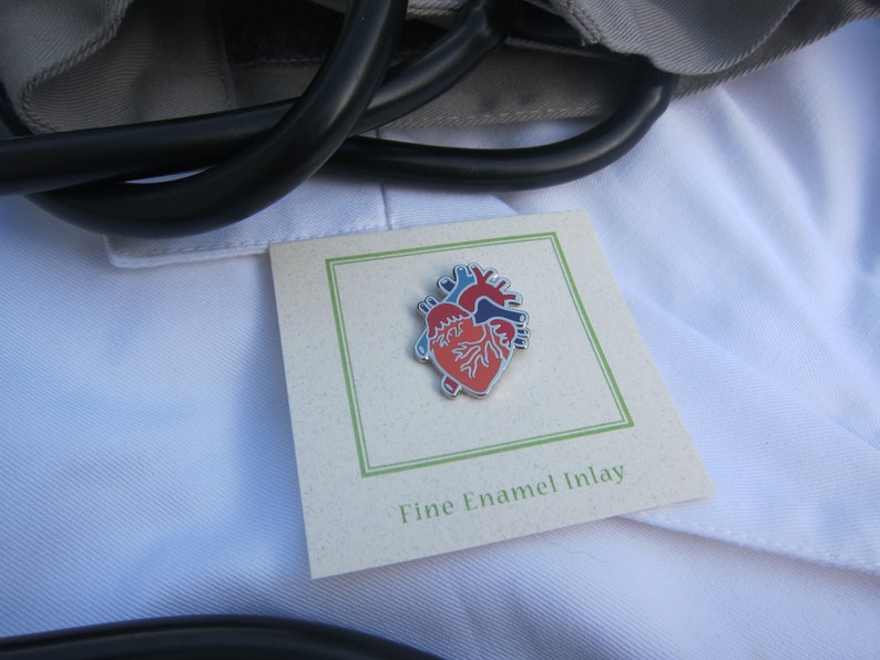 May include: A red, blue and silver enamel heart pin on a white card with the text "Fine Enamel Inlay".