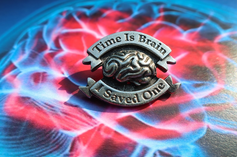 K&ouml;nnte beinhalten: Eine silberne Anstecknadel mit einem Gehirndesign und dem Text "Time Is Brain I Saved One".