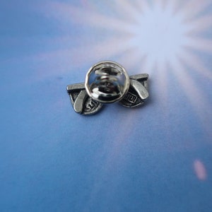 Puede incluir: Pin de tono plateado con un par de gafas de sol con la palabra "Summer" en la lente. El pin tiene un cierre de seguridad en la parte posterior.