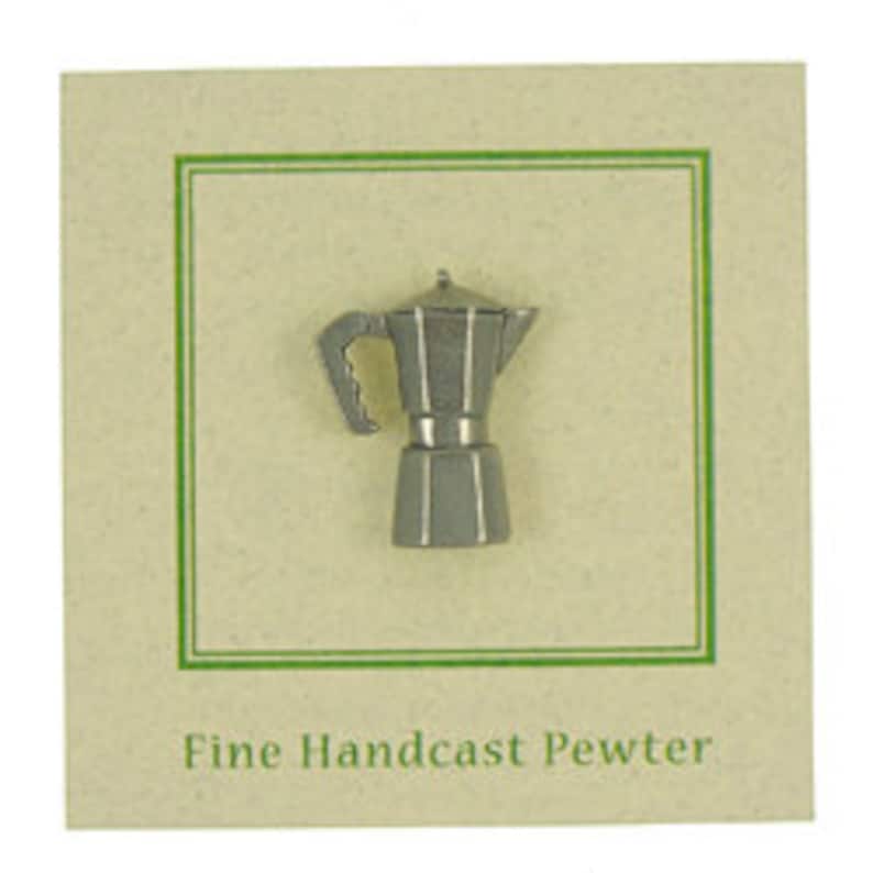 May include: A silver-colored pewter pin shaped like a traditional Italian coffee pot, or Moka pot. The pin is on a small card with the text "Fine Handcast Pewter".