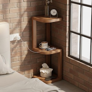 May include: A three-tiered, wooden side table with a curved design. The table holds a coffee cup, a smartphone, a tissue box, and a small clock. The table is next to a bed and a brick wall.