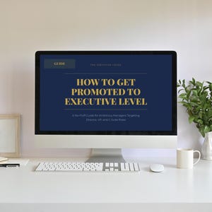 May include: A desktop computer displays a guide titled "How to Get Promoted to Executive Level." The screen has a navy blue background with gold text. A keyboard, mouse, and coffee mug sit on a white desk. A small plant in a vase is also visible.