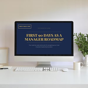 以下が含まれることがあります： デスクトップコンピュータには、紺色の背景に金色のテキストで「First 90 Days as a Manager Roadmap」というタイトルの印刷可能なPDFが表示されています。 コンピュータは、キーボード、マウス、白いマグカップを備えた白い机の上にあります。 小さな植物が白い花瓶に入っています。