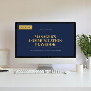 以下が含まれることがあります： デスクトップコンピュータのモニターには、紺色の背景に金色の文字で「MANAGER'S COMMUNICATION PLAYBOOK」と表示されています。画面には「BEST SELLER」と「The complete professional communication guide for leaders」の文字も表示されています。白い机の上には、キーボード、マウス、マグカップがあります。