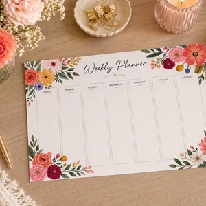 May include: A rectangular weekly planner sheet with a white background, featuring floral illustrations in shades of pink, red, orange, and green at the top left and bottom right corners. The text Weekly Planner is printed in black script at the top.