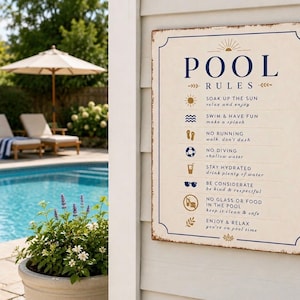 May include: A rectangular off-white sign with dark blue text and gold icons listing pool rules. The text reads POOL RULES, SOAK UP THE SUN, SWIM & HAVE FUN, NO RUNNING, NO DIVING, STAY HYDRATED, BE CONSIDERATE, NO GLASS OR FOOD, and ENJOY & RELAX.