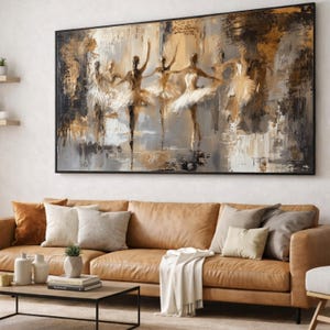 Op de afbeelding: Groot ingelijst abstract schilderij met balletdansers. Het kunstwerk gebruikt een palet van goud, zwart en wit, met zichtbare penseelstreken. Het schilderij hangt boven een bruine leren bank met kussens.