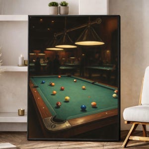 May include: A framed wall art print depicting a dimly lit pool hall with a green felt billiard table in the foreground. Several colourful numbered billiard balls are scattered across the surface. Three pendant lights hang above the table.