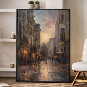 May include: A framed canvas art print depicting a European street scene at dusk. The painting features buildings with warm interior lighting, a wet cobblestone street reflecting the sky's colors, and figures strolling along the sidewalk. The color palette includes muted blues, browns, and oranges.