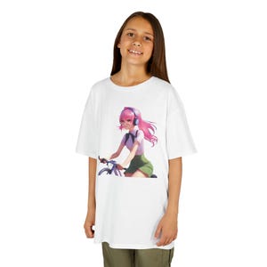 May include: White t-shirt featuring a colorful anime-style illustration of a person with pink hair riding a bicycle. The person is wearing headphones, a white shirt, and a green skirt. The t-shirt is worn by a person.