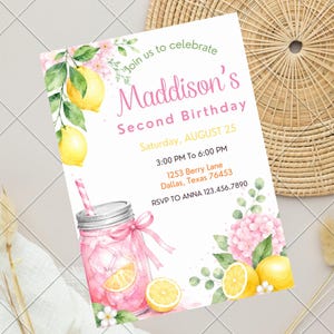 May include: A rectangular birthday invitation card featuring watercolor illustrations of yellow lemons, green leaves, and pink flowers. A pink lemonade mason jar with a straw is at the bottom. Text reads: Join us to celebrate Maddison's Second Birthday.