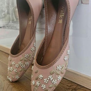 Könnte beinhalten: Ein Paar rosafarbene Ballerinas mit floralen Stickereien und Perlenverzierungen. Die Schuhe haben ein braunes Innenfutter und eine runde Spitze. Die Zahl "36" ist auf der Seite aufgedruckt. Größe 36.