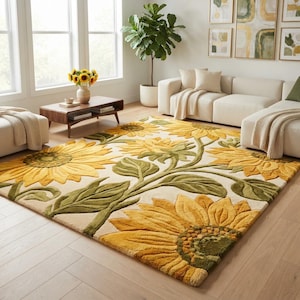 May include: A rectangular area rug featuring a large-scale floral pattern of yellow sunflowers with textured green leaves and stems on a cream-colored background. The rug is positioned on a light wood floor in a room with a sofa and coffee table.