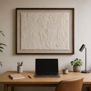 Könnte beinhalten: Ein gerahmtes, rechteckiges Wandkunstwerk mit einer strukturierten, cremeweißen Oberfläche und erhabenen abstrakten Linien, platziert über einem Holztisch mit Laptop, Notizbuch, Stiftehalter, Keramiktasse und einer kleinen Topfpflanze.