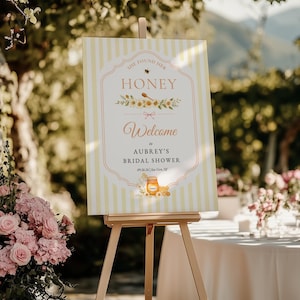 May include: A rectangular welcome sign for a bridal shower featuring yellow and white vertical stripes. The text reads She Found Her Honey, Welcome to Aubrey's Bridal Shower, 09.26.26 | Sea Girt, NJ, with illustrations of a bee, honey dipper, and honey jar.