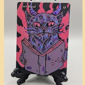 Könnte beinhalten: Eine rechteckige Karte mit einem lila gehörnten Katzenwesen, das ein Buch liest, vor einem leuchtend pinken und schwarzen Hintergrund. Der Text 'Dark Ritual' steht oben links und das Wort 'Kypos' erscheint in einer stilisierten Schrift darüber.