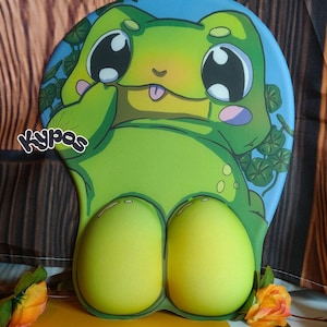 Könnte beinhalten: Eine ergonomische Mausunterlage in Grün und Gelb mit einem Cartoon-Frosch-Design. Die Mausunterlage hat einen blauen Hintergrund mit Kleeblättern und dem Text "Kypas". Der Frosch hat große Augen und einen lächelnden Ausdruck.