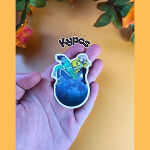 May include: A sticker featuring two anime-style figures sitting on a blue planet. One figure wears a green jacket, the other a yellow jacket. The sticker has the text "Kypas" in a stylized font.