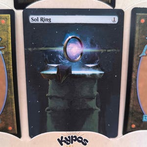 May include: A Magic: The Gathering card featuring the text "Sol Ring" at the top. The card's artwork depicts a glowing ring in a celestial scene, set atop a dark, geometric structure. The card has a white mana symbol in the top right corner.