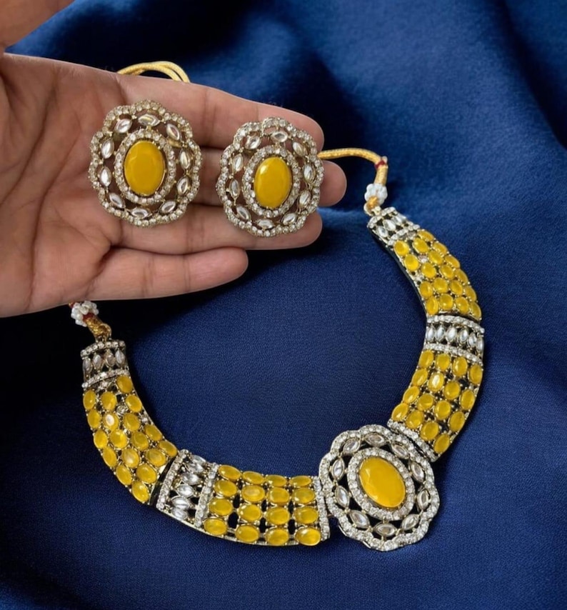 May include: A jewelry set consisting of a necklace and two stud earrings. The necklace features a central oval yellow stone surrounded by clear crystals, flanked by rows of yellow oval stones and clear crystal accents. Matching earrings included.