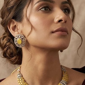 May include: A jewelry set consisting of a necklace and matching stud earrings. The necklace features multiple rows of oval yellow stones accented by small clear stones, with a central floral-shaped pendant. The earrings mirror the floral design.