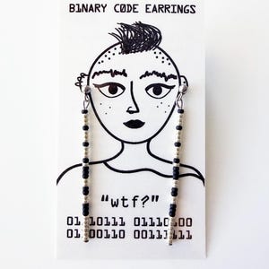 May include: Binary code earrings with black and silver beads hanging from a card with a drawn face and the text "BINARY CODE EARRINGS". The card also has the text "wtf?" and binary code.
