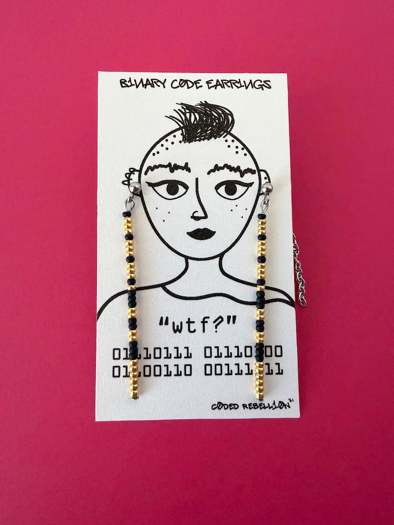 K&ouml;nnte beinhalten: Ohrringe mit goldenen und schwarzen Perlen, pr&auml;sentiert auf einer wei&szlig;en Karte mit einer Zeichnung und Text. Die Karte tr&auml;gt die Aufschrift "BINARY CODE EARRINGS", "wtf?", Bin&auml;rcode und "CODED REBELLION".
