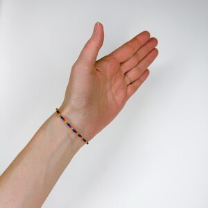 K&ouml;nnte beinhalten: Ein d&uuml;nnes Armband aus kleinen, kugelf&ouml;rmigen Perlen, die in einer sich wiederholenden Regenbogenfarbfolge angeordnet sind, einschlie&szlig;lich Rot, Orange, Gelb, Gr&uuml;n, Blau und Violett, das das Handgelenk mit einem schlichten, leichten Design umschlie&szlig;t.