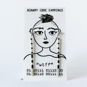 Könnte beinhalten: Ein Paar lange, lineare Ohrringe aus abwechselnd schwarzen und silbernen Perlen, präsentiert auf einer weißen Karte mit einer schwarzen Strichzeichnung eines Gesichts, dem Text "BINARY CODE EARRINGS", "wtf?" und zwei Zeilen Binärcode.
