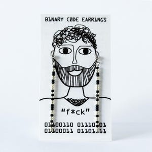 Könnte beinhalten: Ein Paar lange Hängeohrringe mit abwechselnden schwarzen und silbernen Perlen auf einer weißen Karte. Die Karte zeigt den Text "BINARY CODE EARRINGS", eine Strichzeichnung eines bärtigen Gesichts, den Text "f*ck" sowie einen binären Code.