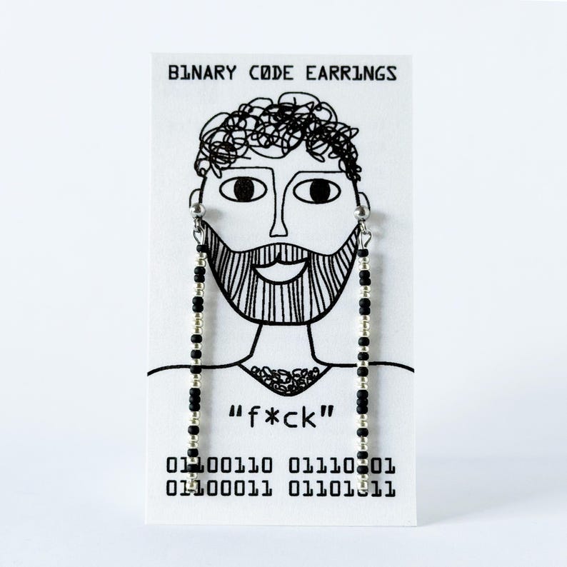 K&ouml;nnte beinhalten: Ein Paar lange H&auml;ngeohrringe mit abwechselnden schwarzen und silbernen Perlen auf einer wei&szlig;en Karte. Die Karte zeigt den Text "BINARY CODE EARRINGS", eine Strichzeichnung eines b&auml;rtigen Gesichts, den Text "f*ck" sowie einen bin&auml;ren Code.