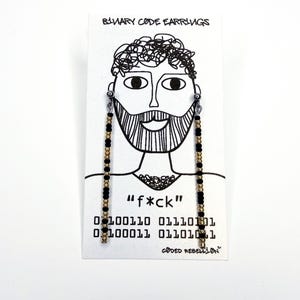 May include: Black and gold beaded earrings hanging from a card with a black and white illustration of a bearded face. The card reads "BINARY CODE EARRINGS" and features the word "f*ck" in quotes, along with binary code.