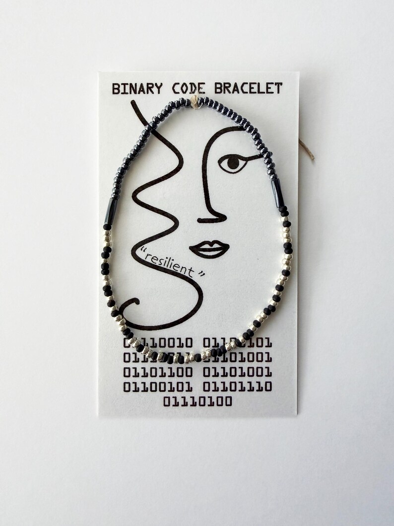 May include: A beaded bracelet featuring alternating black and silver-toned beads on a white display card. The card is printed with the text BINARY CODE BRACELET, a line drawing of a face, the word resilient, and a block of binary code numbers.