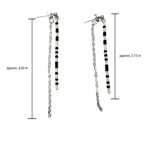 May include: A pair of silver-toned dangle earrings. Each earring features a post with a small cluster of beads, a chain, and a strand of black beads. The earrings are approximately 2.65 inches and 2.15 inches long.