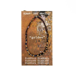 May include: A beaded bracelet on a display card featuring the text BINARY CODE BRACELET, the word golden, and binary sequences. The bracelet consists of small metallic, dark blue, and black beads arranged in a circular pattern on a gold-toned background.