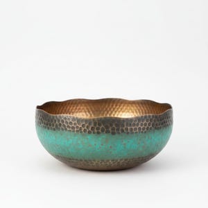 May include: A hammered metal bowl with a wavy rim. The interior is gold, the exterior is a dark bronze color with a turquoise band around the middle. The bowl has a textured surface.