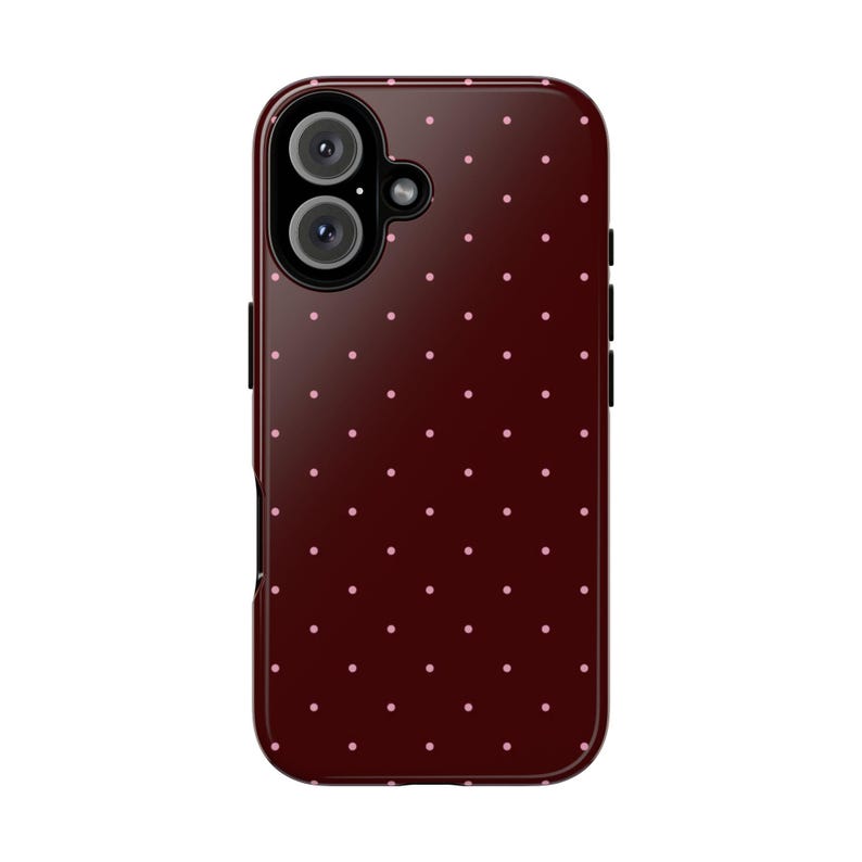 May include: A burgundy phone case with a repeating pattern of small, light pink polka dots. The case has a camera cutout with two lenses and a flash. The case is designed to fit a smartphone.
