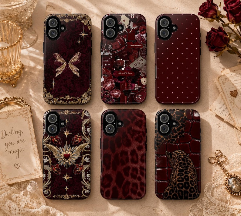 May include: A collection of six phone cases with various designs. The cases feature a deep burgundy color with patterns including a butterfly, floral collage, polka dots, leopard print, and a heart with wings. The cases are arranged on a light-colored surface.