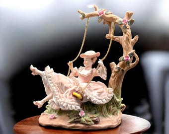 Figura de porcelana de Ardalt Lenwile que representa a una dama victoriana en un columpio con una caja de música Thorens (años 60).