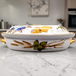 May include: White oval serving dish with a lid, featuring gold trim and handles. The dish is decorated with illustrations of lemons, plums, and wheat. The word "Beer" is written on the side of the dish.