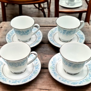 May include: Four white teacups and saucers with a blue and green floral pattern. The cups and saucers have a silver trim.