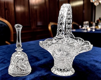 Puede incluir: Una campana de cristal tallado transparente y una cesta a juego de cristal tallado transparente. Ambos artículos presentan intrincados patrones geométricos y motivos de aves grabados. La campana tiene un asa delgada y base.