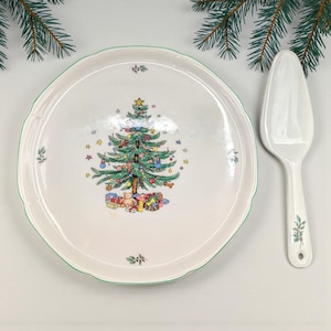 May include: A white ceramic Christmas serving plate with a green scalloped edge, featuring a decorated Christmas tree design. Includes a matching pie server. Festive holiday tableware.