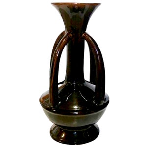 May include: A dark brown ceramic vase with a wide base and a narrow neck. The vase has four handles that extend from the neck and curve down to the base.