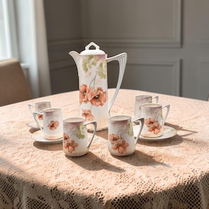 May include: A porcelain coffee set featuring a tall lidded pitcher and four matching mugs on saucers. The white ceramic pieces are decorated with painted orange poppy flowers and green foliage, accented with delicate silver-toned trim details.