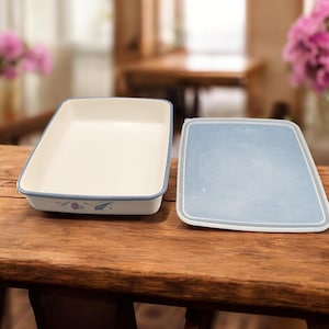 May include: Off-white rectangular ceramic baking dish with a light blue floral design and a matching lid. The dish has a light blue trim and is placed on a wooden surface. The lid is light blue with a white trim.