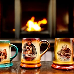 May include: Three ceramic mugs with different designs. Each mug features a person in a medieval setting. The mugs are brown, green, and orange.