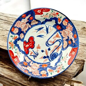 May include: A decorative ceramic plate with a blue rim and intricate floral and abstract designs in red, orange, and blue. The plate features a white background with detailed patterns, showcasing a blend of artistic elements.